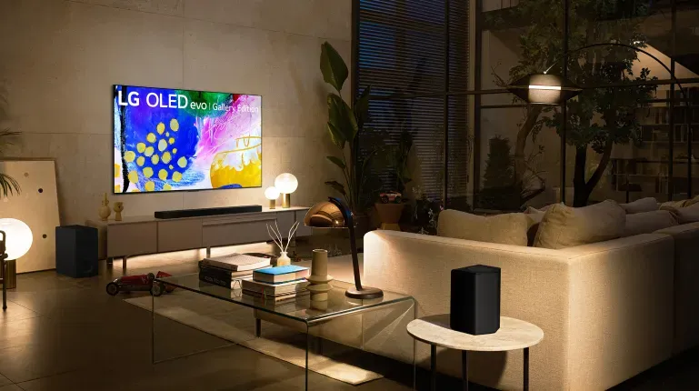 A dark living room with a lot of ambient lighting from various lamps, featuring a large LG OLED flat screen TV